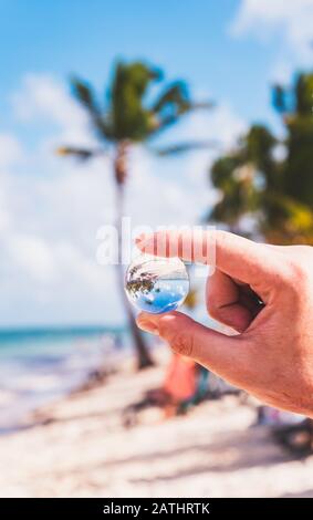 Main De La Personne Qui Tient Mini Boule De Verre Et Fond De Plage Banque D'Images