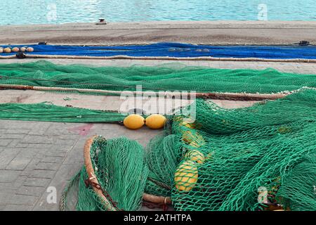 Filets de pêche bleus et verts avec flotteurs jaunes posés sur le sol au port avec mer en arrière-plan Banque D'Images