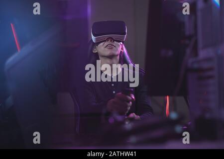 Vue en petit angle chez un jeune homme asiatique portant un casque VR lors de la lecture de jeux vidéo à l'aide d'un décalage de course dans un espace de copie cybernétique sombre Banque D'Images