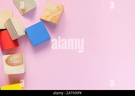 Jouets en bois pour enfants sur un fond rose concept zéro ouest. Cadre à partir du développement de cubes colorés. Espace de copie. Vue du dessus, disposition plate. Banque D'Images