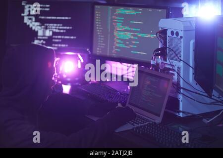 Vue latérale d'un pirate non reconnaissable utilisant un équipement informatique avec code de programmation sur les écrans dans la salle sombre, concept de cyber-sécurité, espace de copie Banque D'Images