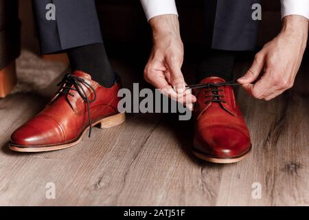 groom a attaché les lacets sur les chaussures de gros plan. homme d'affaires pendre des chaussures à l'intérieur dans la chambre d'hôtel. mains du mans et paire de chaussures en cuir pour homme. réunion de Banque D'Images