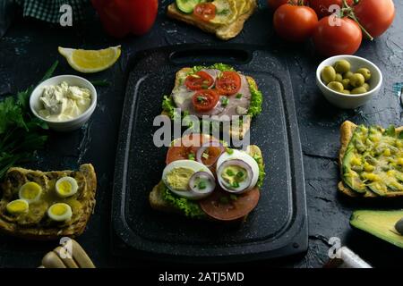 Planche à découper grise avec sandwichs au jambon, à la laitue et aux tomates et sandwich aux tomates, aux œufs et aux oignons violets Banque D'Images
