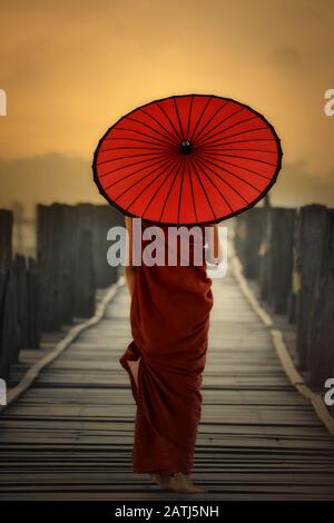 Myanmar Novice moine et tenant un parapluie rouge marchant sur le pont U - Bein Mandalay Birmanie. Banque D'Images