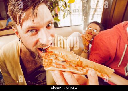 Un jeune gars avec une barbe morde un grand morceau de pizza closeup. Des amis se fêtes au pub. Gros plan portrait Banque D'Images