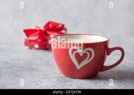 Tasse rouge de café Latte avec lait et cadeau sur fond gris. Saint-Valentin ou invitation d'anniversaire. Gros plan. Banque D'Images