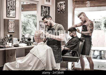 Barbiers donnant la coupe de cheveux dans le salon de coiffure Banque D'Images