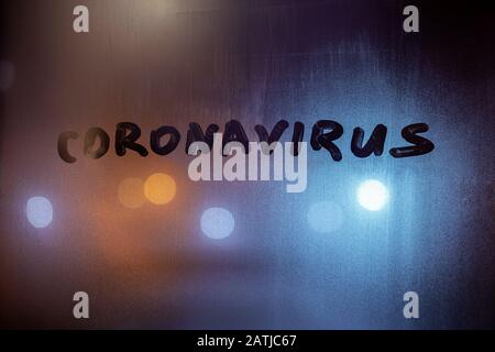 le mot coronavirus écrit à la main sur le verre brumeux de nuit dans des couleurs bleu-orange. Banque D'Images