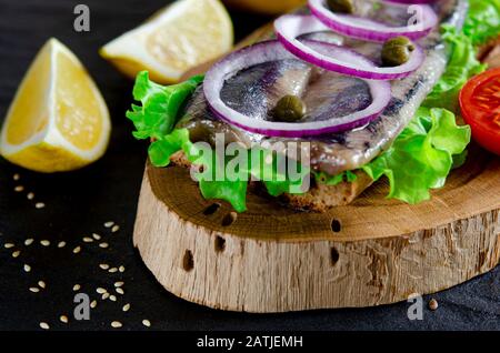Le smorrebrod appétissant avec le hareng norvégien, la laitue, l'oignon bleu, le citron et la tomate se trouve sur une planche en bois Banque D'Images