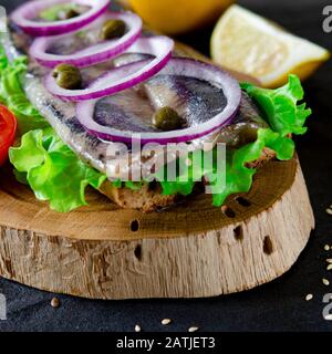 Le smorrebrod appétissant avec le hareng norvégien, la laitue, l'oignon bleu, le citron et la tomate se trouve sur une planche en bois Banque D'Images