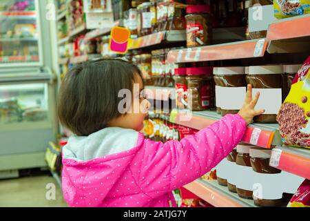 Petite fille veut acheter du chocolat au comptoir dans le supermarché Banque D'Images