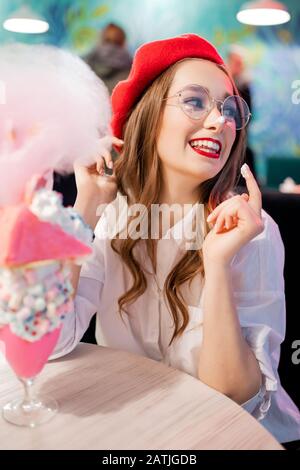 Dessert sucré avec bonbons en coton rose, milkshake et gâteau. Fille en béret rouge et verres, café en France Banque D'Images