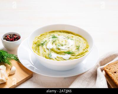 grand bol blanc avec soupe de crème verte végétale de brocoli, courgettes, pois verts sur fond blanc, vue latérale Banque D'Images