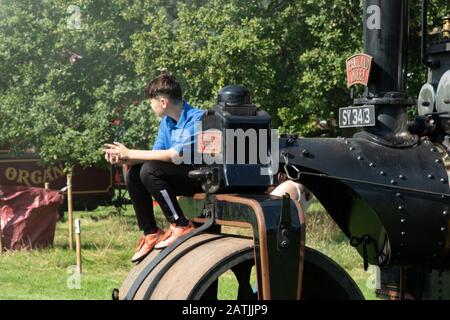 Jeune homme adolescent adulte assis sur un classique Fowler Road Roller, Harewood Steam Rally, West Yorkshire, Angleterre, Royaume-Uni. Banque D'Images