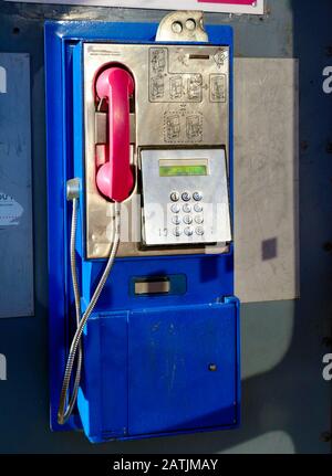 vue avant de l'ancien téléphone public de style rétro bleu à pièces avec clavier à bouton-poussoir, récepteur rose et étiquettes d'instructions Banque D'Images