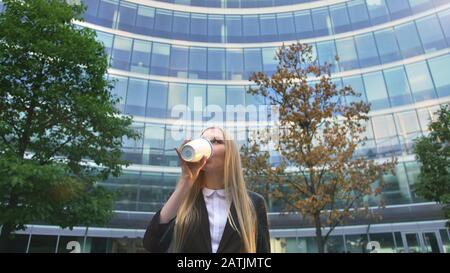 Par en dessous de la blonde woman in suit le café dans la tasse de papier à l'écart sur rue. Banque D'Images