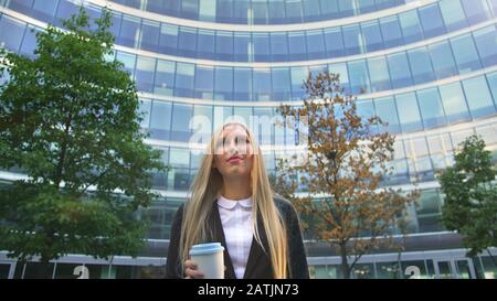 Par en dessous de la blonde woman in suit le café dans la tasse de papier à l'écart sur rue. Banque D'Images