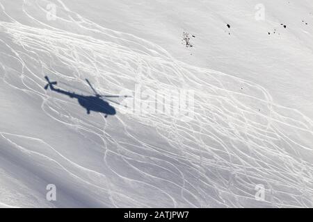 Ombre d'un hélicoptère sur une piste de ski hors piste enneigée avec des traces de skis et de snowboards le jour ensoleillé de l'hiver. Heli-ski dans les hautes montagnes. Banque D'Images