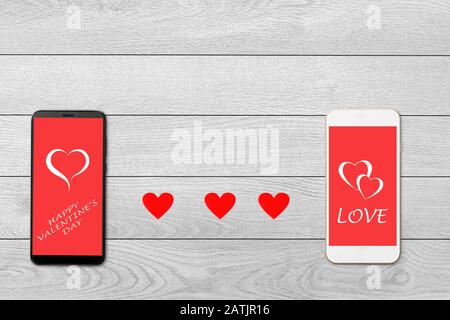 Concept de Saint-Valentin, sur fond de bois blanc isolé coeurs de papier rouge et deux smartphones, salutation sur l'écran du smartphone Banque D'Images