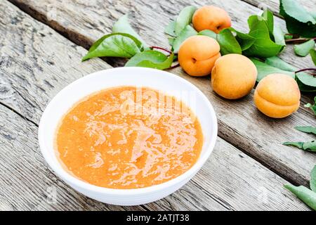 Confiture biologique maison dans un bol blanc et abricots mûrs sur une table en bois. Gros plan. Banque D'Images