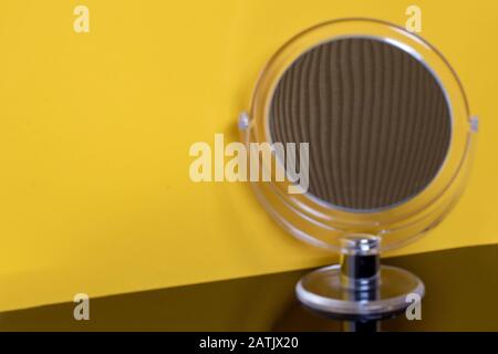 Gros plan d'un miroir cosmétique rond transparent avec focalisation sélective sur le centre de la réflexion agrandie d'une surface en métal ondulé sur yello Banque D'Images