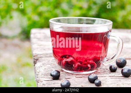 Tasse de thé aux fruits en verre avec des baies de cassis sur une table en bois en plein air. Gros plan. Banque D'Images