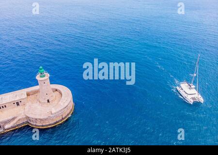 Le catamaran à bateaux blanc entre dans le port à côté du phare contre la mer bleue avec des vagues. Vue de dessus, concept de voyage Banque D'Images