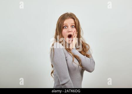 la femme en chandail gris est choquée par les nouvelles touche main à joue ouvre la bouche Banque D'Images