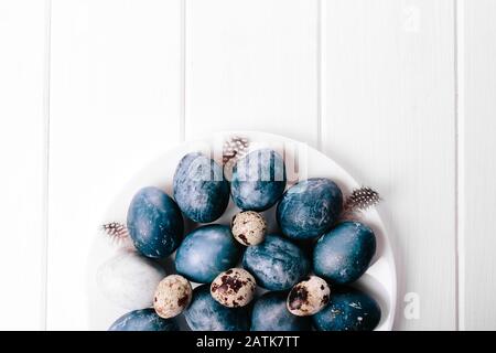 Beau groupe ombre bleu oeufs de Pâques avec des œufs de caille et des plumes sur un fond en bois blanc. Concept de Pâques. Œufs de bordure. Espace de copie pour le texte. Couleur bleu classique de l'année 2020 Banque D'Images