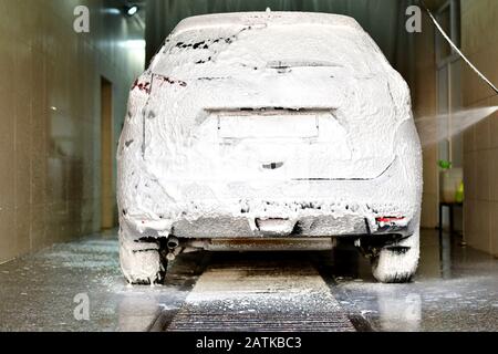 La voiture est recouverte de mousse et de spray destiné au corps dans la pièce pour laver les voitures. Banque D'Images