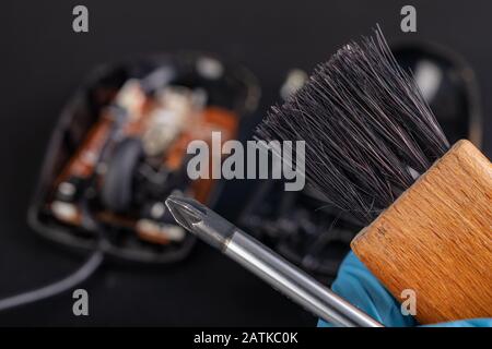 Nettoyage d'une souris d'ordinateur optique à l'aide d'une brosse. Garder l'espace de travail de l'ordinateur propre. Fond sombre. Banque D'Images