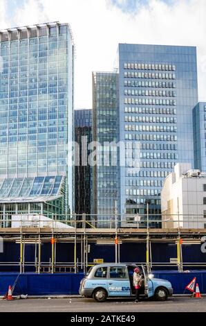 Un chauffeur de taxi de dame arrive dans son taxi qui est garé devant les travaux de construction étant porteur dehors sur des blocs de bureaux modernes. Banque D'Images