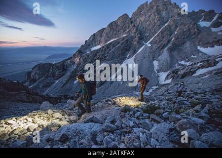 Trois randonneurs avec des lumières marchent le long d'un sentier dans les Tetons, lever du soleil Banque D'Images