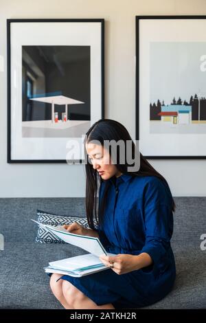 Jeune femme d'affaires lisant des documents tout en étant assis sur un canapé au bureau Banque D'Images