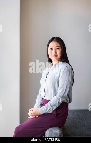 Portrait d'une femme d'affaires souriante avec des mains claquées assis sur un canapé contre le mur au bureau Banque D'Images