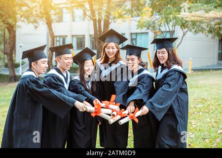 les étudiants heureux titulaires de diplômes sur le campus universitaire sont titulaires de diplômes Banque D'Images