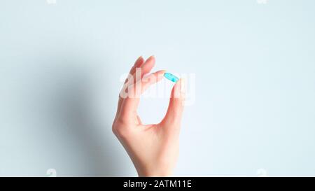 Main féminine tenant la capsule de la pilule médicale sur fond bleu. Concept de pharmacie et de médecine Banque D'Images