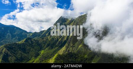 Vue d'en haut, vue imprenable aérienne d'une chaîne de montagnes verdoyante entourée de nuages et d'un beau ciel bleu en arrière-plan. Sembalun, Lombok. Banque D'Images