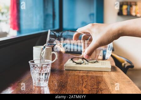 La main de l'homme verse de l'eau fraîche du pichet dans un verre dans le café. Banque D'Images