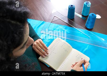 belle couturière avec de longs cheveux écrit dans un carnet. le tailleur crée une collection de tenues. jeune femme design vêtements note des idées dans note Banque D'Images