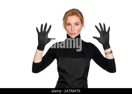 une femme blonde en gants de latex médical noirs pose sur un fond blanc isolé. une femme en vêtements sombres d'un employé du salon de beauté. le concept d'hygiène et de protection Banque D'Images