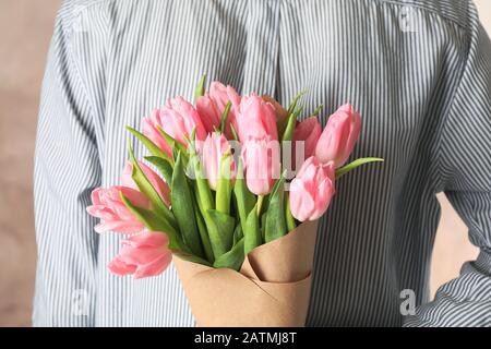 Homme tenant bouquet de tulipes derrière son dos sur fond brun, gros plan Banque D'Images