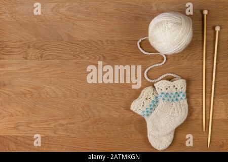 Tricotage de l'arrière-plan. Aiguilles à tricoter en bois, boule de fil et petites chaussettes tricotées en laine sur fond en bois Banque D'Images