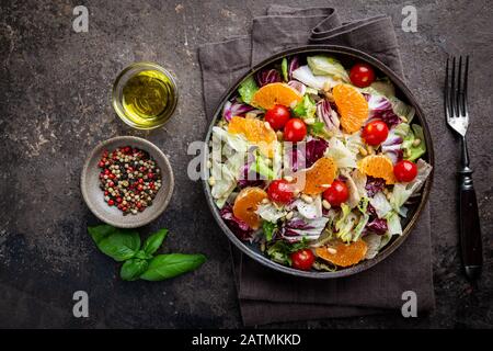 Salade verte fraîche feuilles de frisee, radicchio et laitue d'agneau avec tomate, olives et mandarine dans une assiette, vue de dessus. Banque D'Images