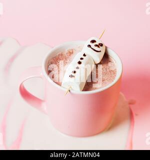 Chocolat chaud avec bonhomme de neige marshmallow dans un mug rose sur un fond rose Banque D'Images