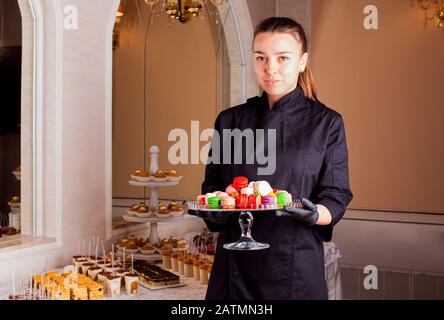 Le serveur sert un stand de macarons colorés à la table douce. Banque D'Images