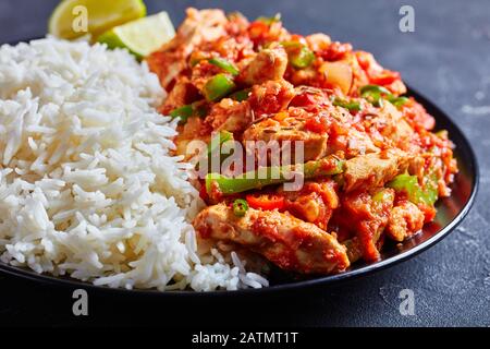 dinde frisées cuites avec légumes et sauce tomate servies avec riz long à la vapeur et tranches de citron vert sur une plaque, vue horizontale d'en haut, clos Banque D'Images