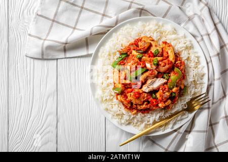 dinde rasée de légumes et de sauce tomate servie avec du riz long grain à la vapeur et des tranches de citron vert sur une plaque blanche sur une table en bois, horizontale Banque D'Images