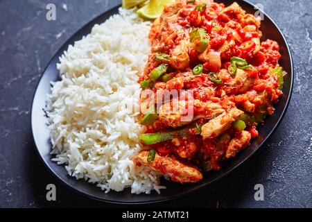 gros plan des bandelettes de dinde gardiées de légumes et de sauce tomate servies avec du riz long grain à la vapeur et des tranches de citron vert sur une assiette, vue horizontale de Banque D'Images