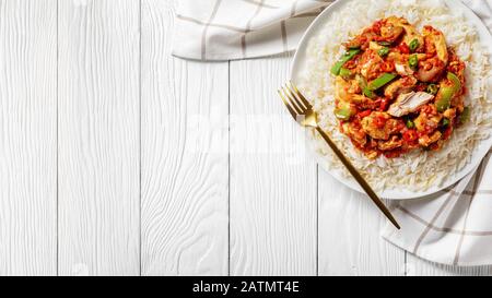 dinde frisées garnies de légumes et sauce tomate surmontée sur riz cuit à la vapeur à grains longs sur une plaque blanche sur une table en bois, vue horizontale d'en haut, c Banque D'Images